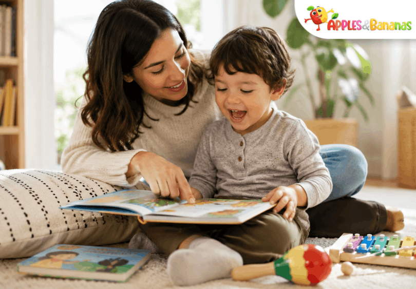 A smiling toddler reads a colorful picture book with a parent in a cozy playroom, with musical toys nearby to show how stories and songs support early language development.